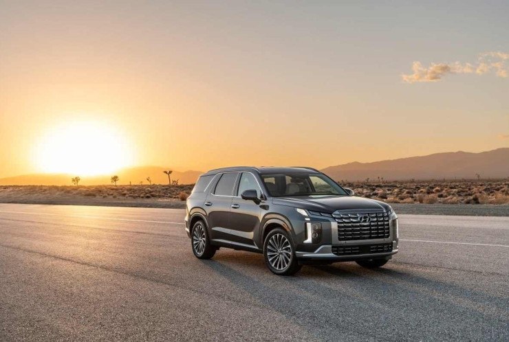 Hyundai Palisade 2024 cinza escuro de frente estático no asfalto com por do sol ao fundo